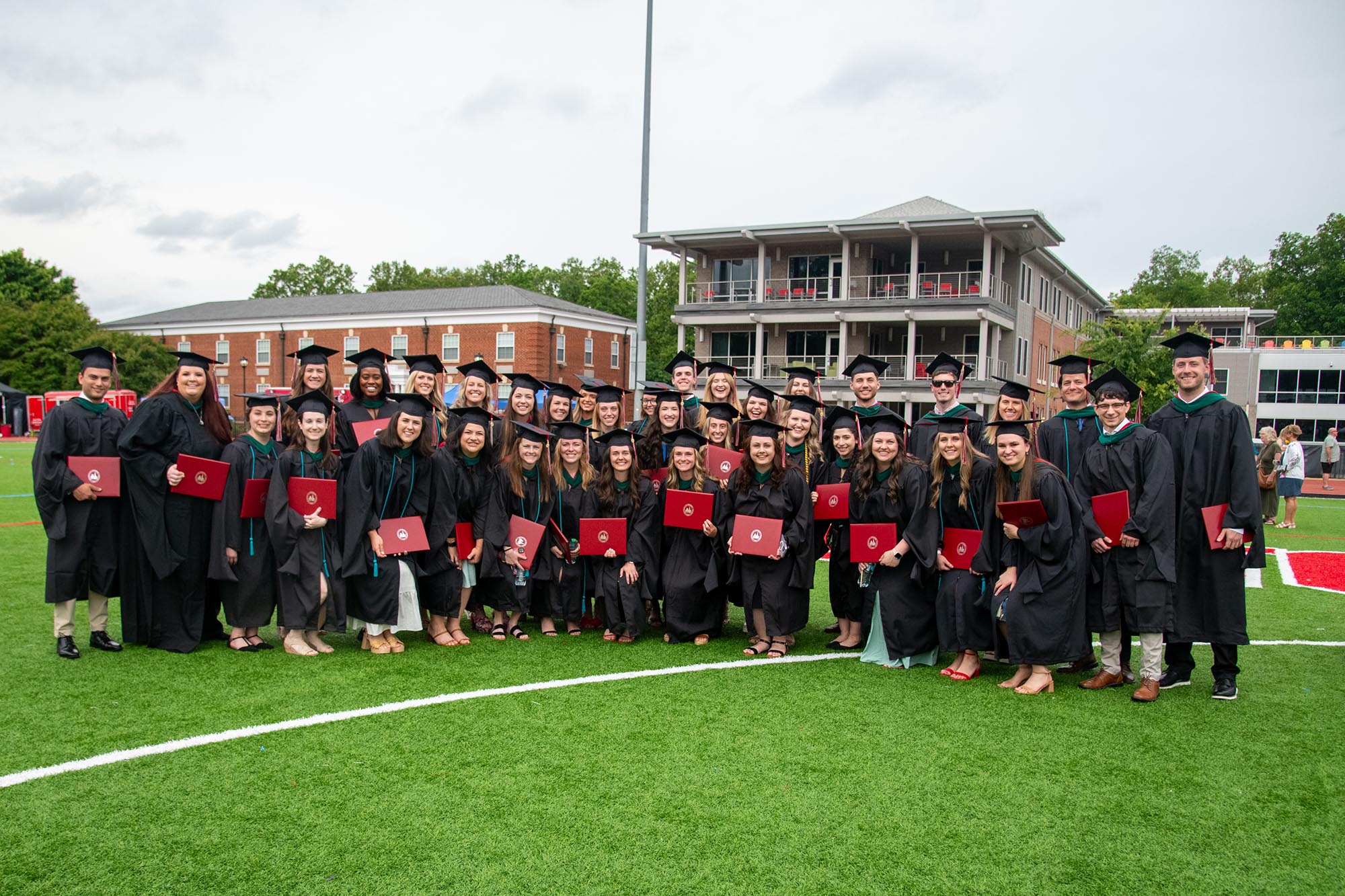 A group of master's level graduates in their regalia on a sports field. 