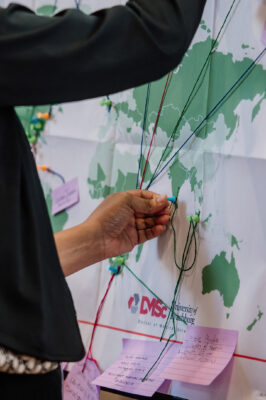 A woman adds a pin to and string to a world map.