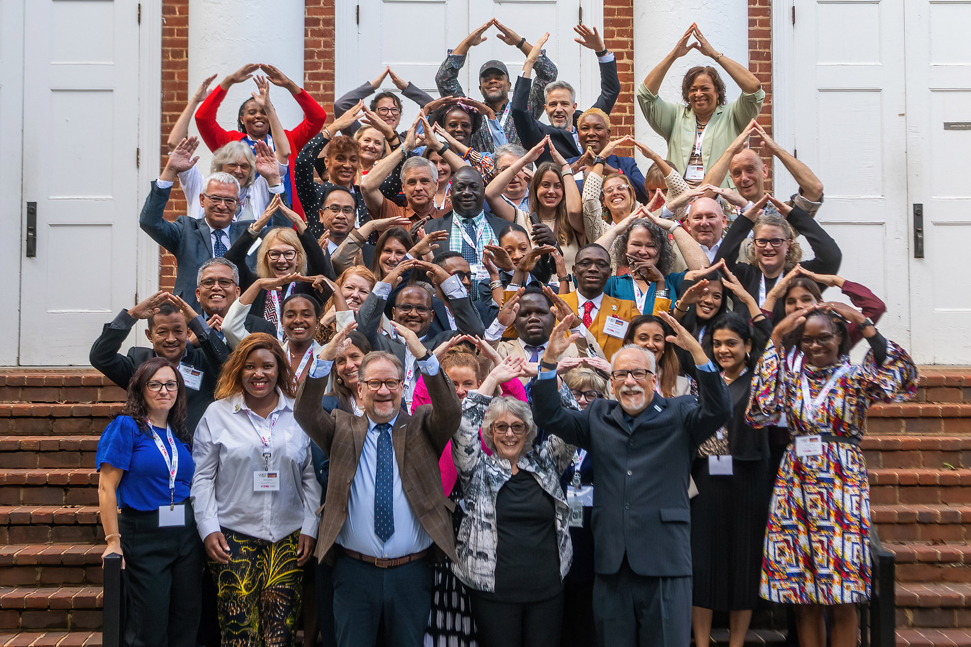 Conference attendees pose for group photo in front of Hall Campus Center with arms raised above their heads.