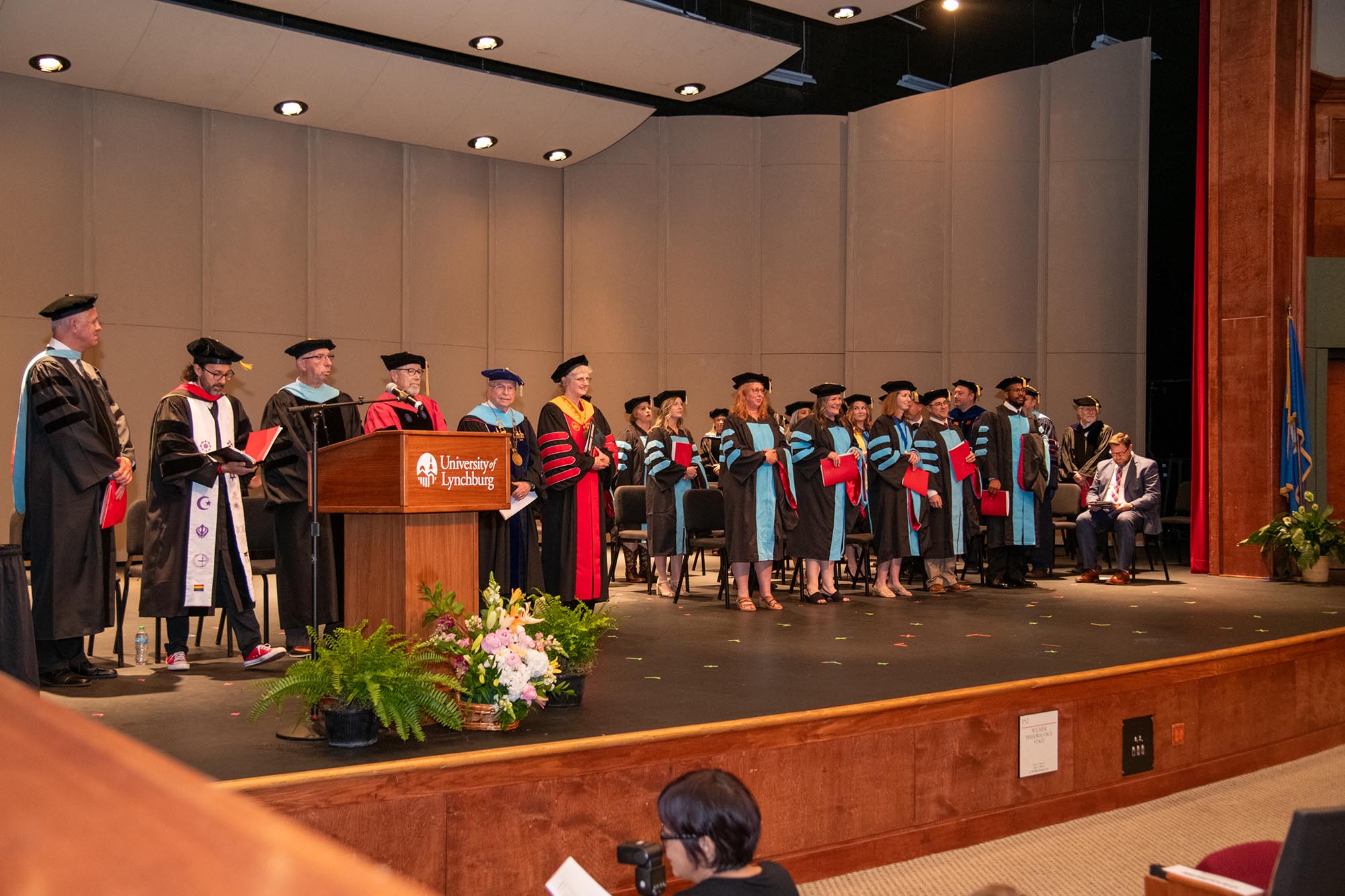 Doctoral candidates and faculty stand on a stage for graduation.