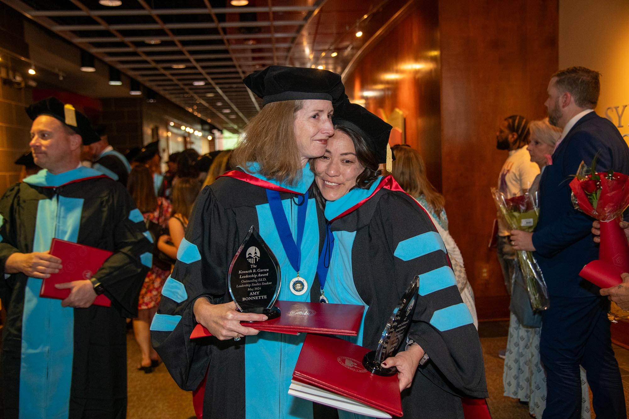 Two women in doctorate regalia embrace.