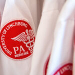 Close up on PA white coats and the red and white patches with the caduceus and text that reads"University of Lynchburg PA Medicine."