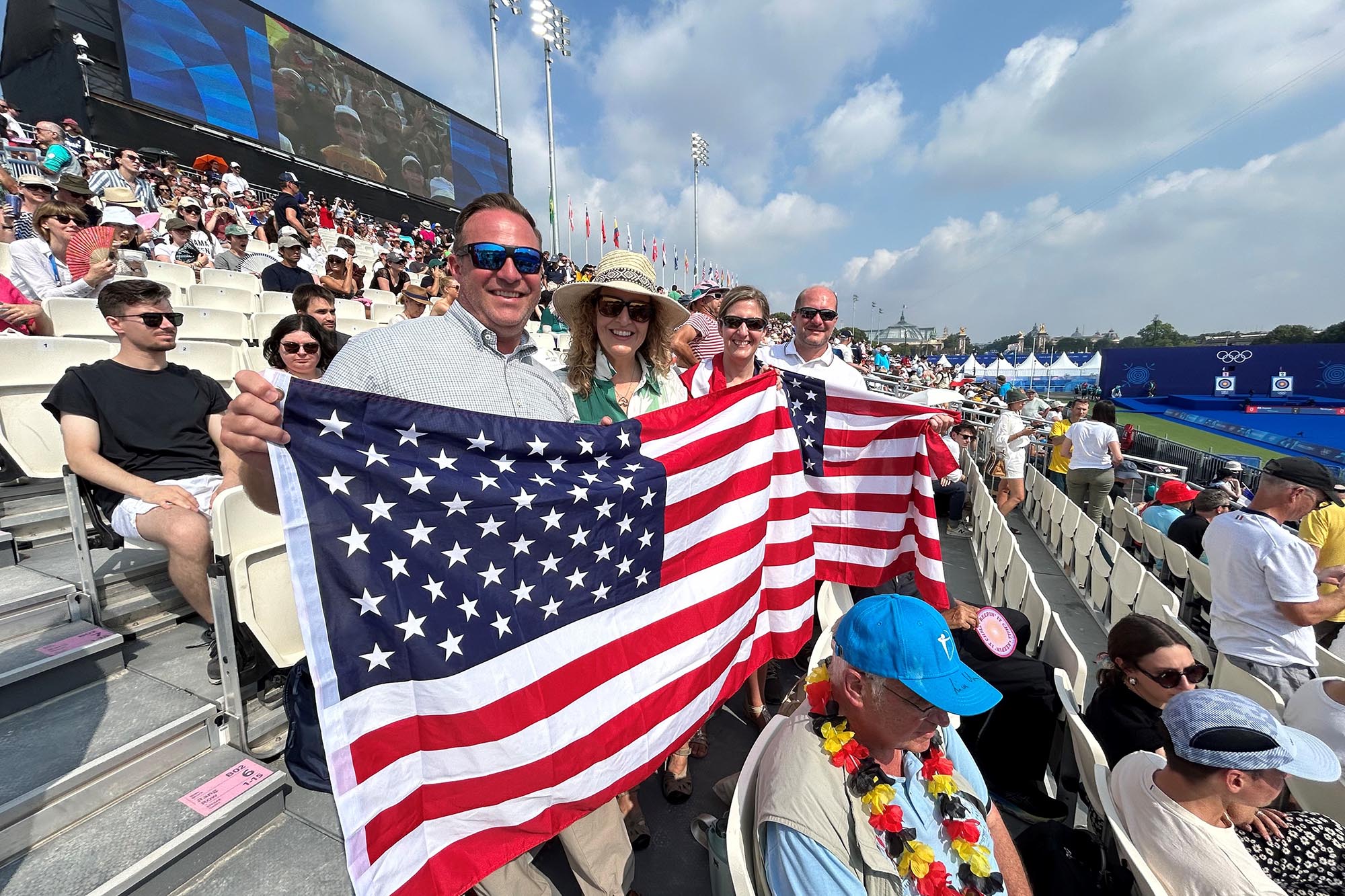 A group holds two American flags while standing in a crowded stadium. 