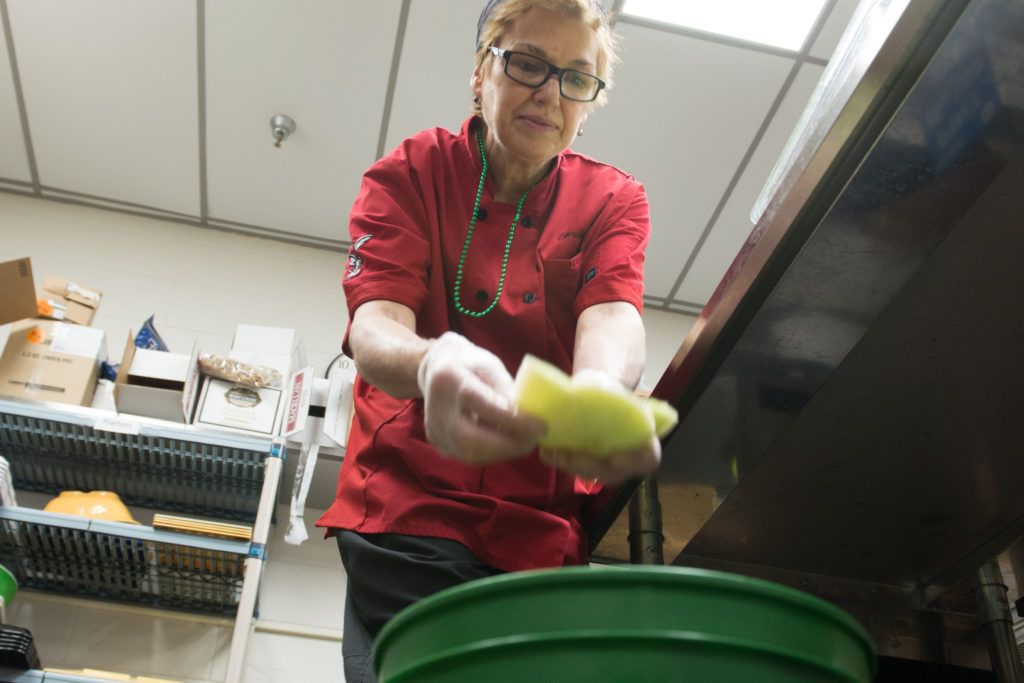 Dining services employee drops food scraps into a green bucket for compost