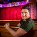 Dustin Williams sitting in a theatre with the stage in the background